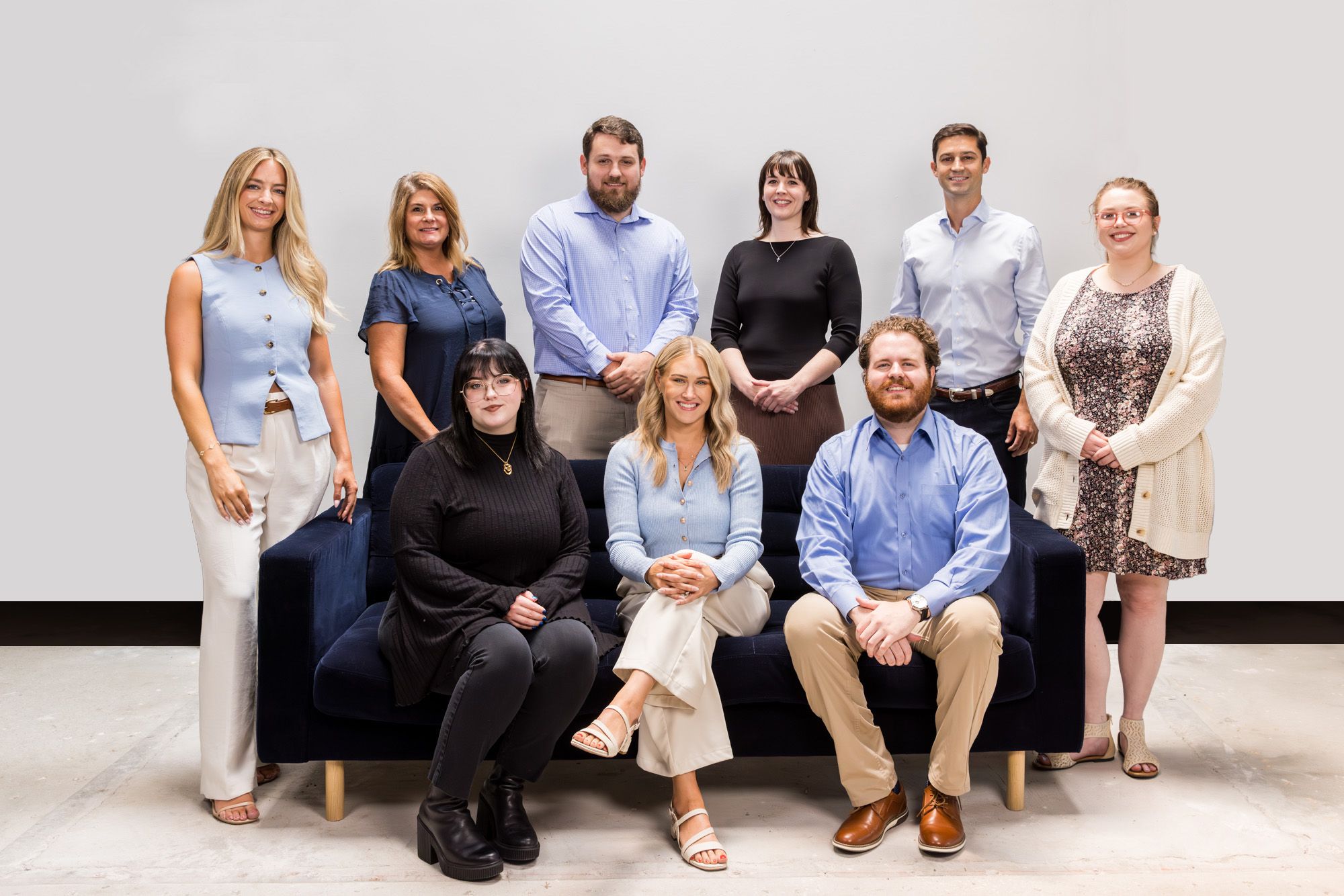 Group of eight adults posing for a photo in a casual office setting, standing and seated on a navy sofa.